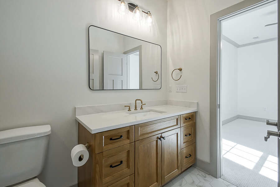 Bath vanity with quartz top, wood cabinetry and brushed-brass fixtures