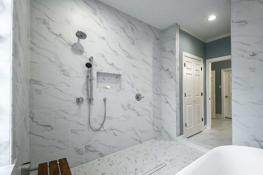 Walk-in shower with handheld sprayer and built-in niche in marble tile